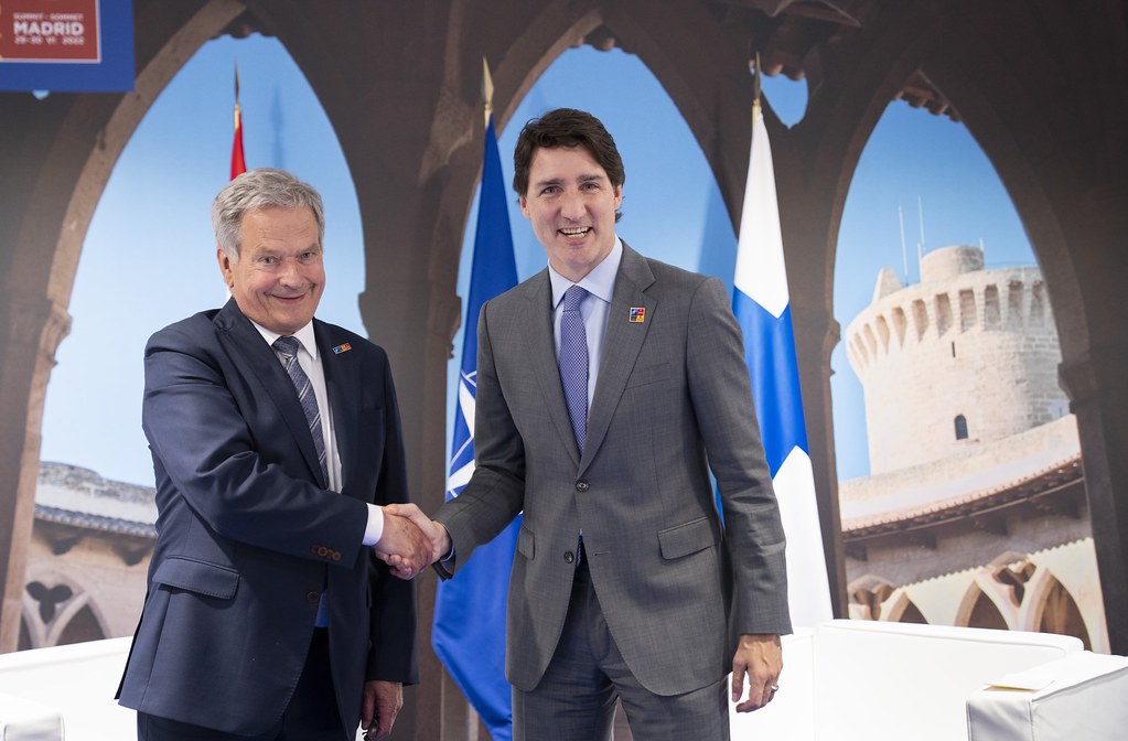 Two men shaking hands in front of flags.